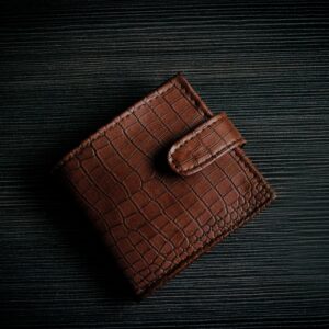 A stylish brown leather wallet with a textured design lies on a dark surface, showcasing its elegant craftsmanship.