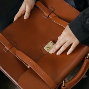Close-up view of hands handling a stylish brown leather briefcase, perfect for business settings.