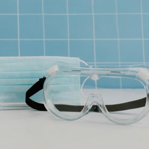 Close-up of protective goggles and a medical face mask against a tiled background.